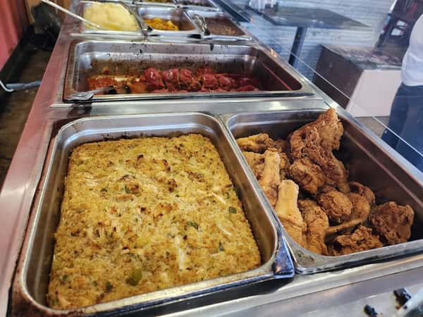 Hot food buffet featuring cornbread dressing, fried chicken, meatballs in sauce, and various vegetable sides.