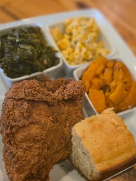 Classic Southern soul food plate featuring a piece of crispy fried chicken, collard greens, baked macaroni and cheese, candied yams, and a slice of cornbread.