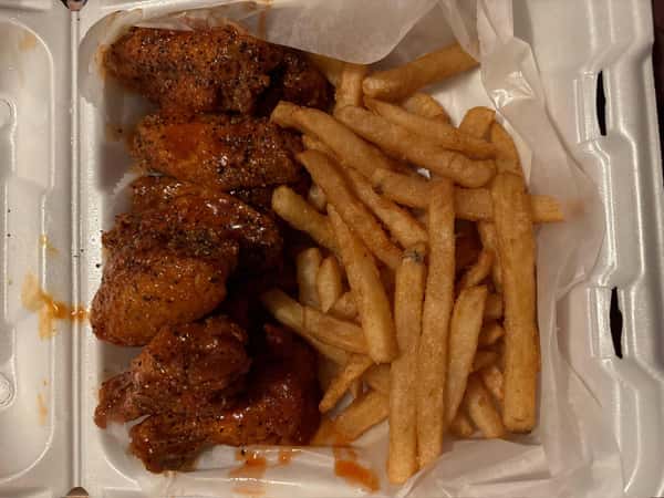 Takeout container with seasoned buffalo wings and a serving of crispy French fries on parchment paper.