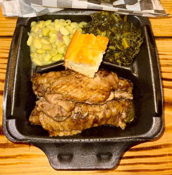 Southern-style meal with stewed turkey wings, collard greens, lima beans with sausage, and cornbread in a black takeout tray.