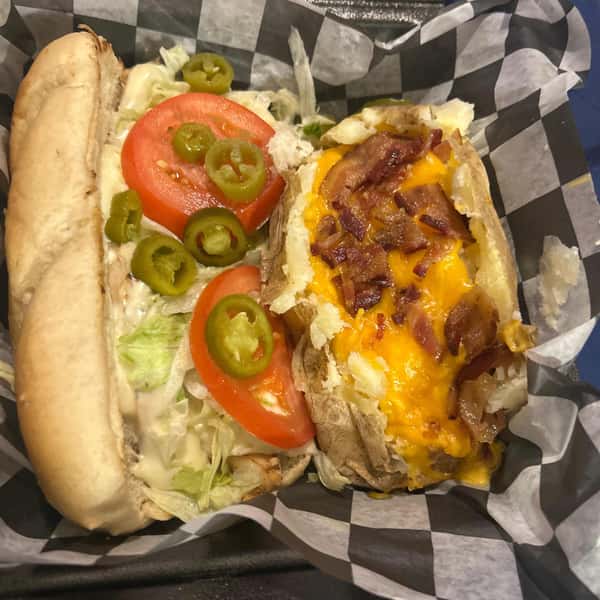 Grilled chicken sandwich with lettuce, tomato, jalapeños and sauce, served alongside a loaded baked potato topped with cheese and bacon.