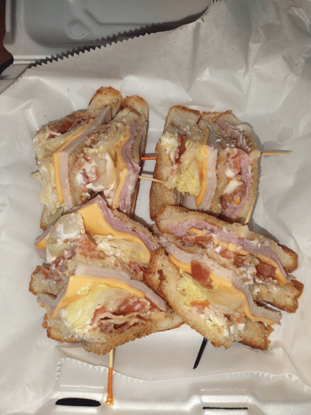 Stacked club sandwich quarters with layers of ham, turkey, cheddar cheese, lettuce, tomato, and mayo on toasted bread.