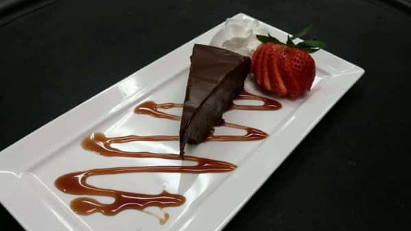 Slice of chocolate cake on a platter with a side of strawberry slices