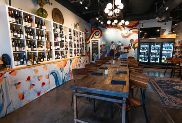 Rustic communal dining table next to the extensive white wine wall and colorful mural at The Downing Bottles & Bites.