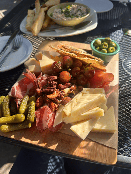 Charcuterie board with cured meats, cheese, and pickles served on a sunny patio table at The Downing Bottles and Bites.