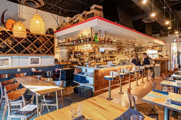Rustic and industrial interior of The Downing Bottles and Bites, showcasing the brightly lit full bar, cubby wine rack, and warm wooden dining tables.