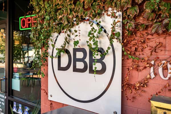 The Downing Bottles and Bites (DBB) logo sign on a red wall, framed by changing autumn ivy and a neon Open sign.