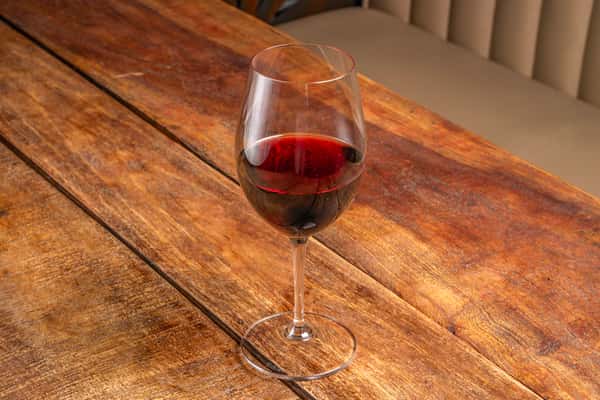 Deep red wine in a stemmed glass resting on a rustic wood table at The Downing Bottles and Bites.