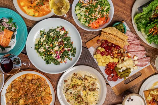 Diverse overhead dining spread featuring charcuterie, salmon, vibrant salads, and pasta dishes with wine glasses at The Downing Bottles and Bites.