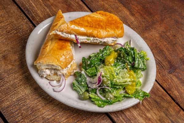 Golden sub sandwich with creamy filling and a side of crisp green Italian salad with pepperoncinis, served at The Downing Bottles and Bites.