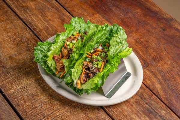 Two vibrant green lettuce wraps appetizer from The Downing Bottles and Bites, served on a white plate atop a rustic brown wood table.