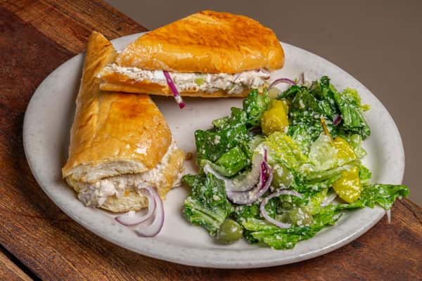 Golden chicken salad sandwich and a crisp side salad with olives and pepperoncini peppers, available at The Downing Bottles and Bites.