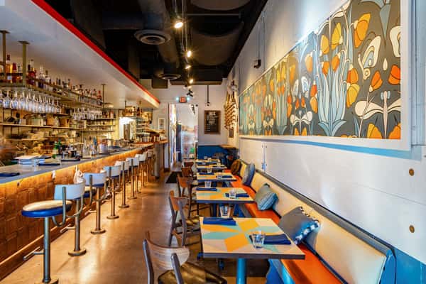 Vibrant interior of The Downing Bottles and Bites with bar seating, orange booths, and a bold floral mural dominating the dining room wall.