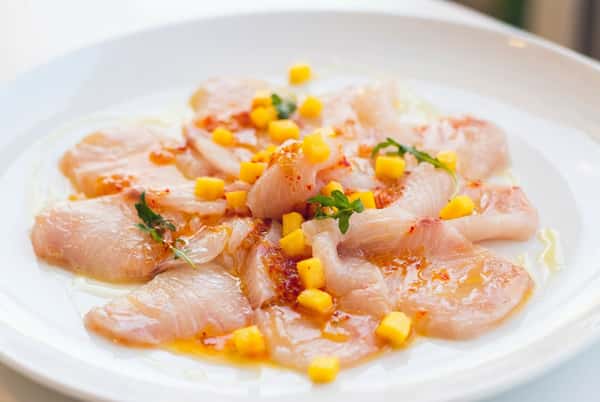 Thinly sliced fish plated with sweetcorn and garnish