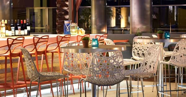 Outdoor restaurant patio with stylish metal dining chairs, candlelit tables, and a welcoming open-air seating area at a modern hotel restaurant.