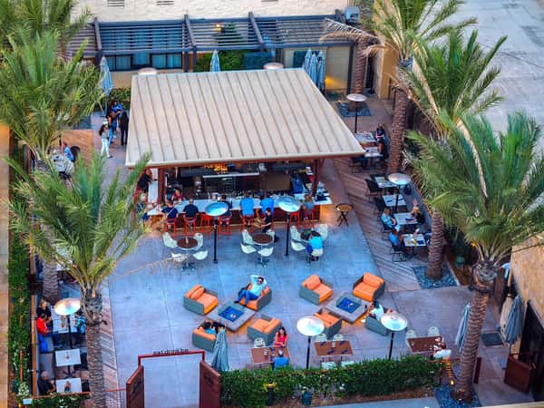 Aerial view of a vibrant outdoor restaurant patio with colorful seating, open-air bar, and lively dining atmosphere at a modern hotel.
