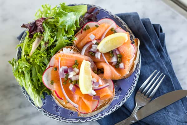 A colorful smoked salmon dish is plated with care, topped with fresh herbs, thin lemon slices, and delicate edible flowers. Served alongside a crisp green salad, the presentation is bright, elegant, and full of fresh flavors.