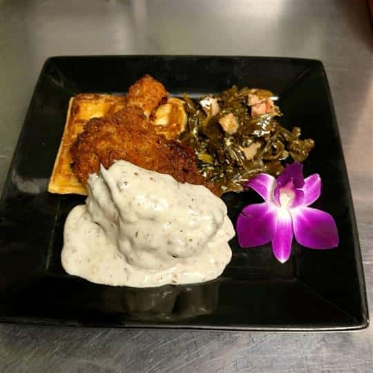 Meat topped with gravy with a side of collard greens