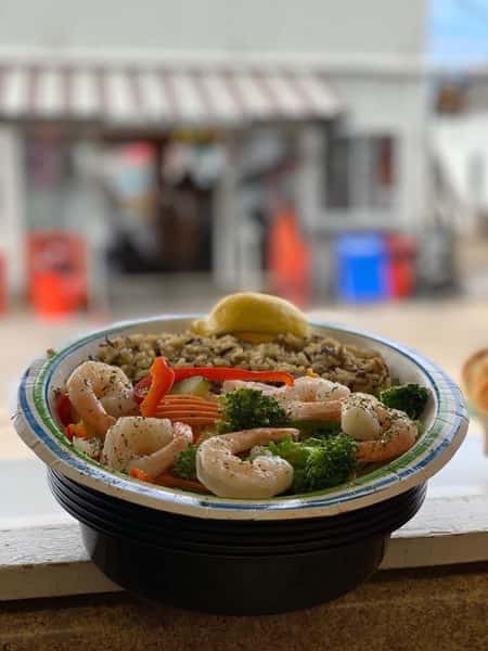 shrimp, broccoli, and veggies in a bowl over rice in front of a window