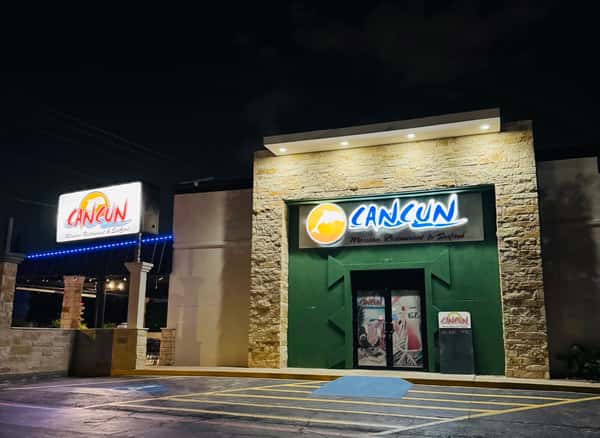 Exterior night view of Cancun Mexican Restaurant & Seafood featuring illuminated signage, stone façade, and a warmly lit entrance, showcasing a welcoming ambiance.