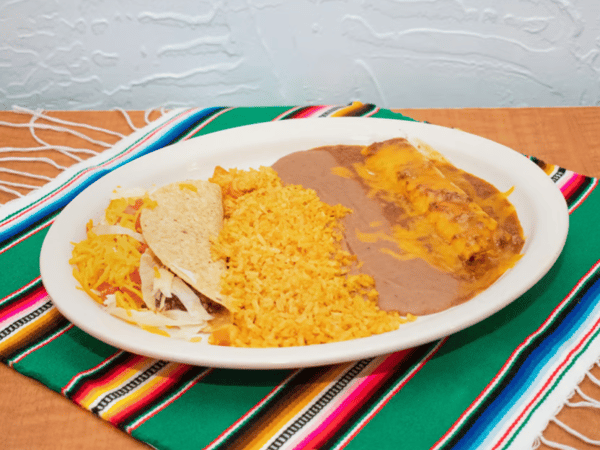 Classic Mexican combination plate featuring a cheese enchilada smothered in enchilada sauce, refried beans, seasoned Mexican rice, and a beef taco with shredded lettuce and cheese, all on a festive tablecloth.