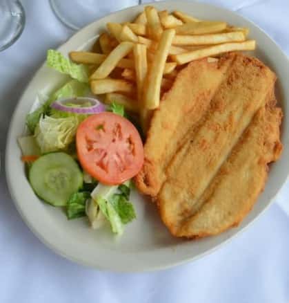 Crispy breaded fish fillet served with golden French fries and a side salad of fresh lettuce, cucumber, tomato, and onion on a white plate.