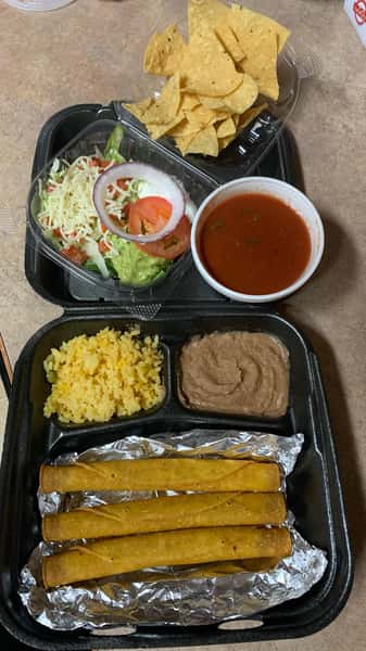 Mexican takeout platter with crispy taquitos, refried beans, yellow rice, shredded lettuce, guacamole, and a side of chips and salsa.