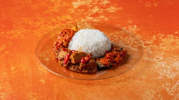 Authentic Malaysian rice plate with white rice, spicy sambal, and traditional side dishes served on a vibrant orange background.