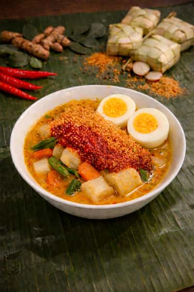 Traditional Malaysian lontong with rice cakes, vegetables, hard-boiled egg, and spicy sambal in a flavorful coconut curry broth.