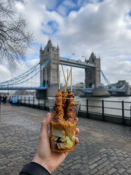 Grilled Malaysian chicken satay skewers with peanut sauce, photographed in front of London Tower Bridge for a vibrant street food scene.