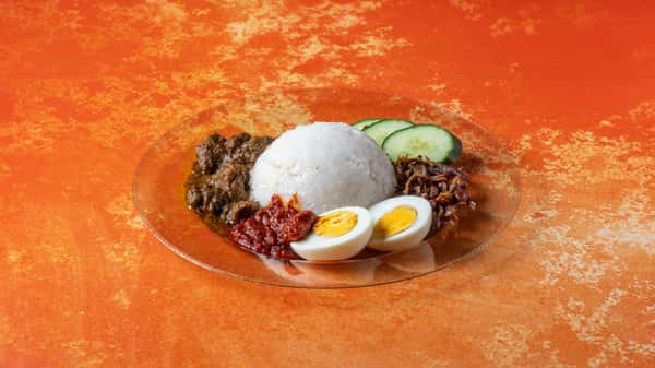 Classic Malaysian nasi lemak with coconut rice, sambal, boiled egg, cucumber slices, anchovies, and traditional accompaniments.