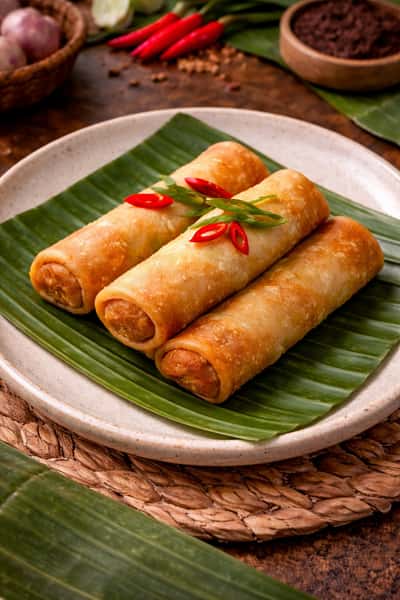 Crispy golden spring rolls served on a banana leaf with fresh chili garnish, a classic Southeast Asian appetizer.