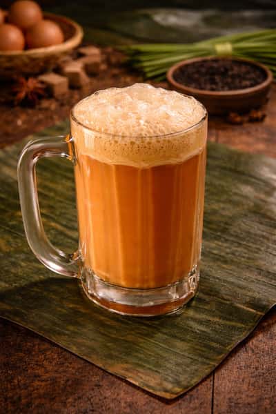 Traditional Malaysian teh tarik with a rich frothy top served in a glass mug on a rustic wooden table.