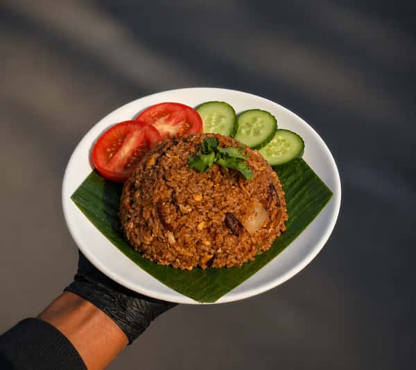 Malaysian-style nasi goreng fried rice topped with crispy shallots and served with fresh cucumber and tomato slices.