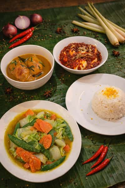 Traditional nasi lemak platter with crispy fried chicken, coconut rice, sambal, boiled egg, peanuts, anchovies, and fresh cucumber slices served on a banana leaf.