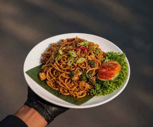 Authentic Malaysian mee goreng stir-fried noodles with vegetables, savory seasoning, and fresh cucumber and tomato garnish.