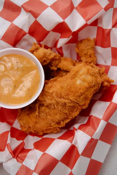 Close up of a crispy chicken tender served with creamy dipping sauce.
