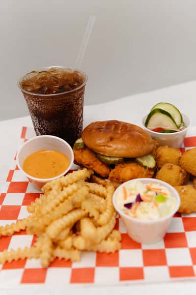 Chicken sandwich meal served with fries, hush puppies, coleslaw, dipping sauce, and a soft drink.