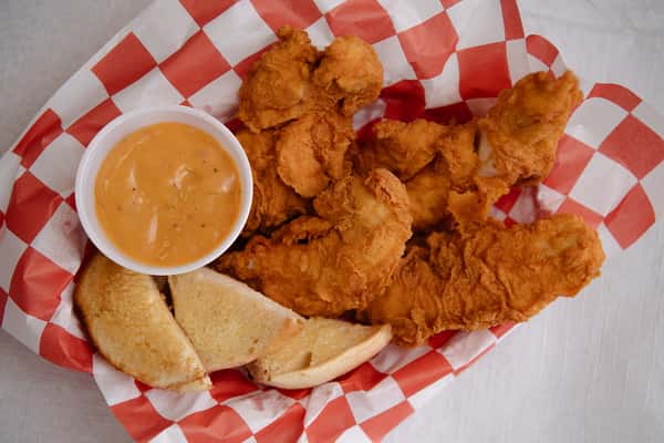 Basket of crispy chicken tenders served with cornbread and dipping sauce.