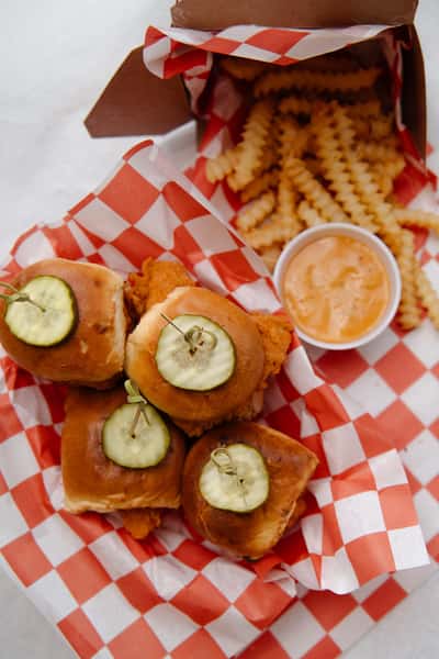 Basket of chicken sliders topped with pickle slices and served with dipping sauce.