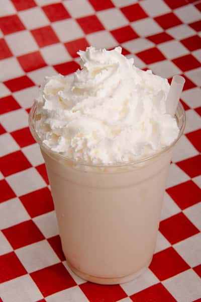 Vanilla milkshake topped with whipped cream in a clear cup.