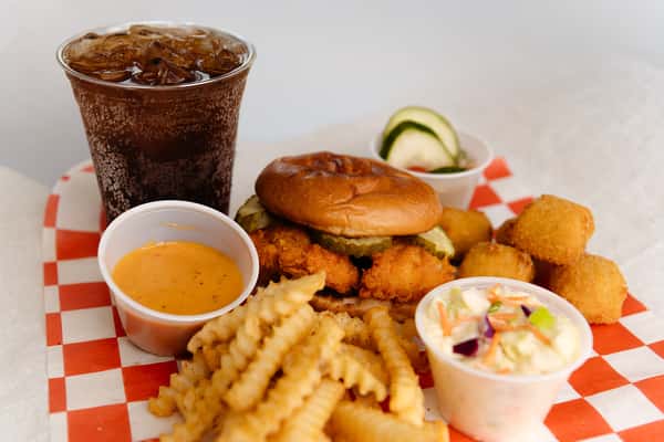 Chicken sandwich combo served with fries, hush puppies, coleslaw, dipping sauce, and a soft drink.