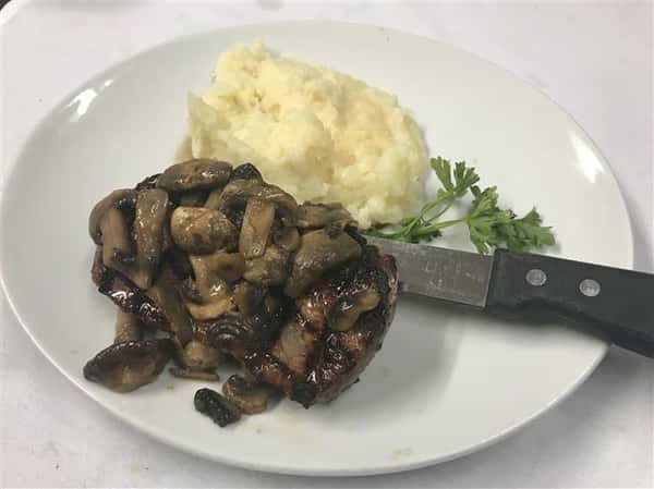 Steak covered with mushrooms and side of mashed potatoes.