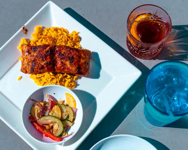 Top down view of a plated fried entrée with dipping sauce and a blue drink nearby.