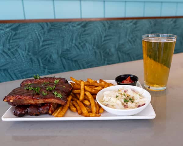 Ribs served with fries and a dipping cup, with a glass of beer beside the plate.