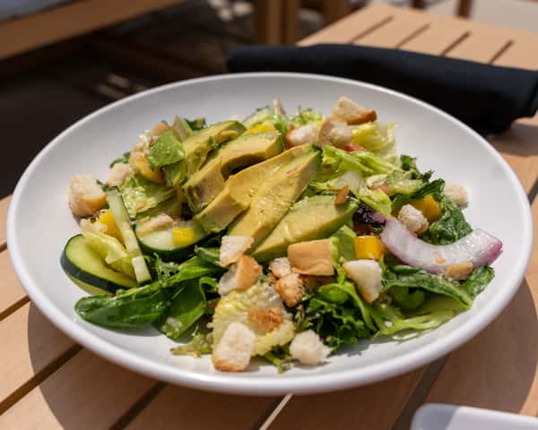 Salad topped with sliced avocado on a white plate.