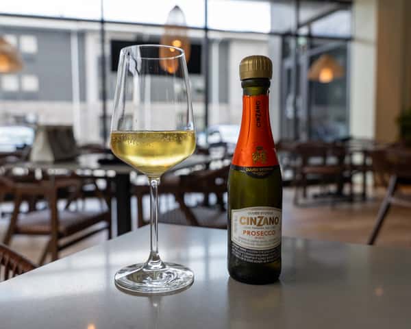 Bottle of sparkling wine on a table in a dining room with chairs in the background.