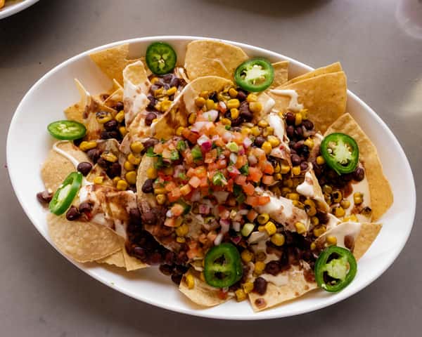 Plate of loaded nachos topped with chopped vegetables and sliced jalapeños.