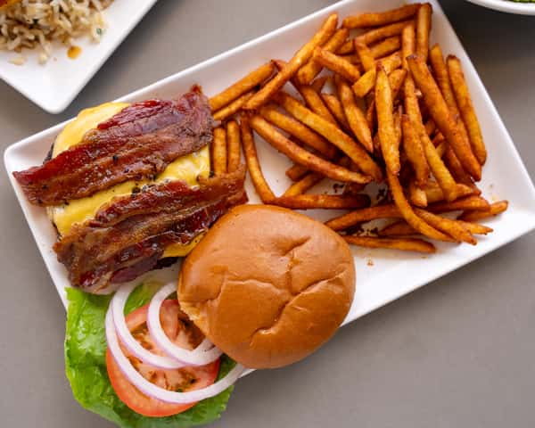 Burger on a bun served with fries on a white plate.