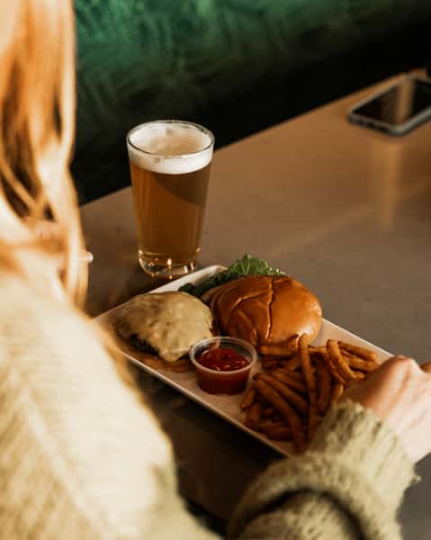 guest sitting next to plate with burger fries and a beer